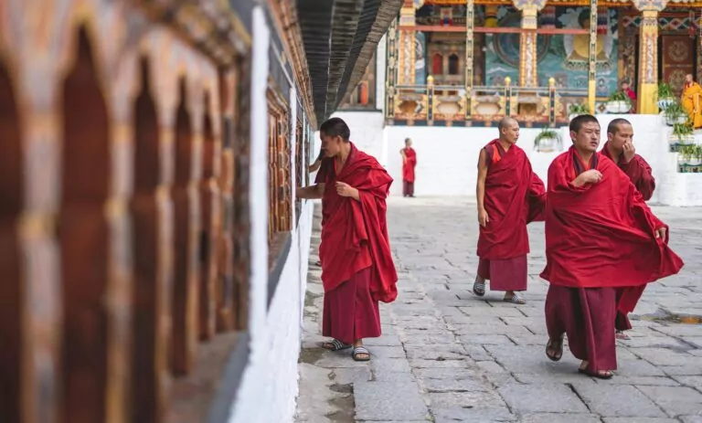 Buddhist monks in red robes walking and interacting in a Bhutan temple courtyard.