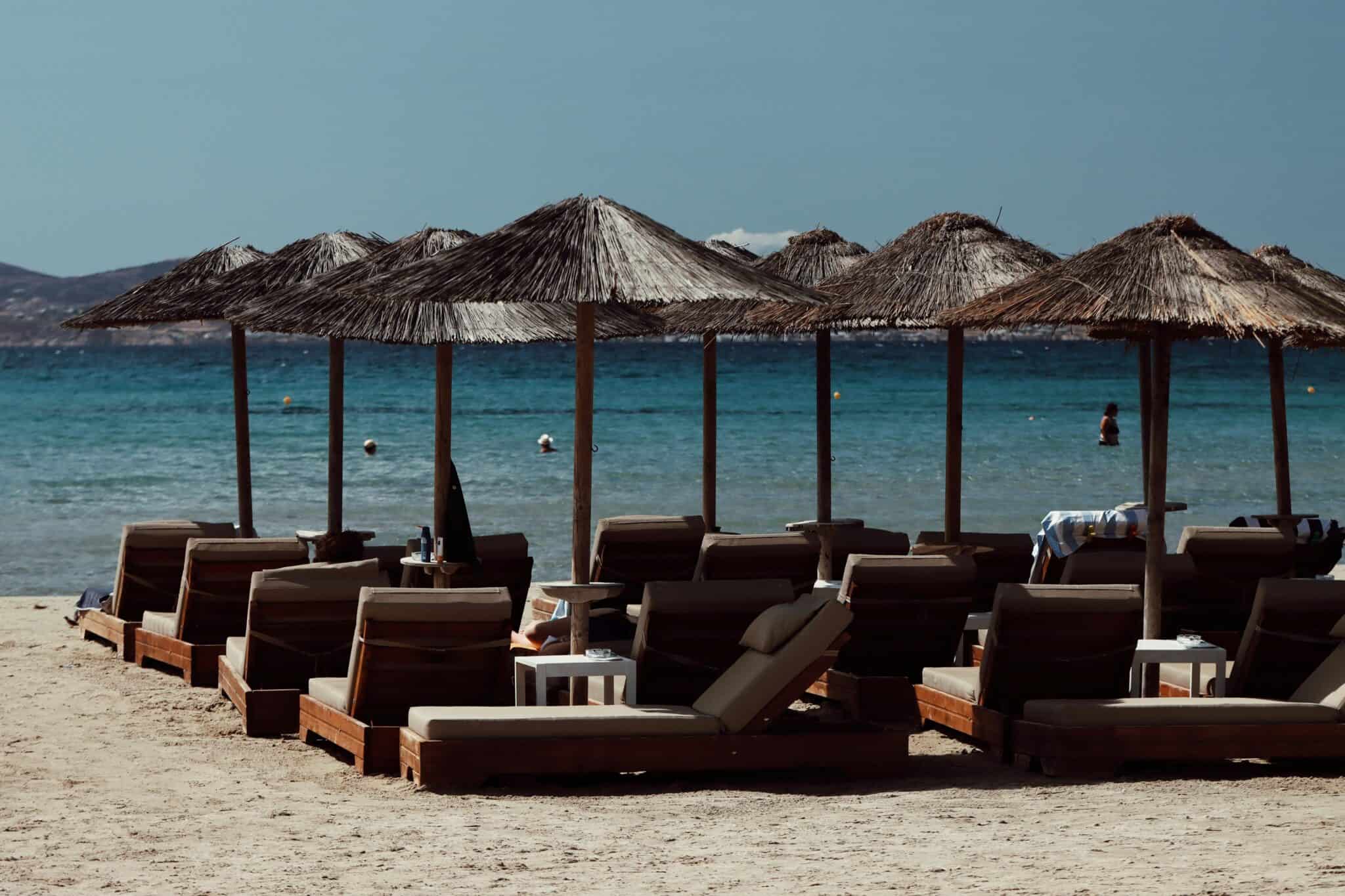 Beach loungers and umbrellas on a sandy shore in Naxos, Greece, under a clear blue sky.