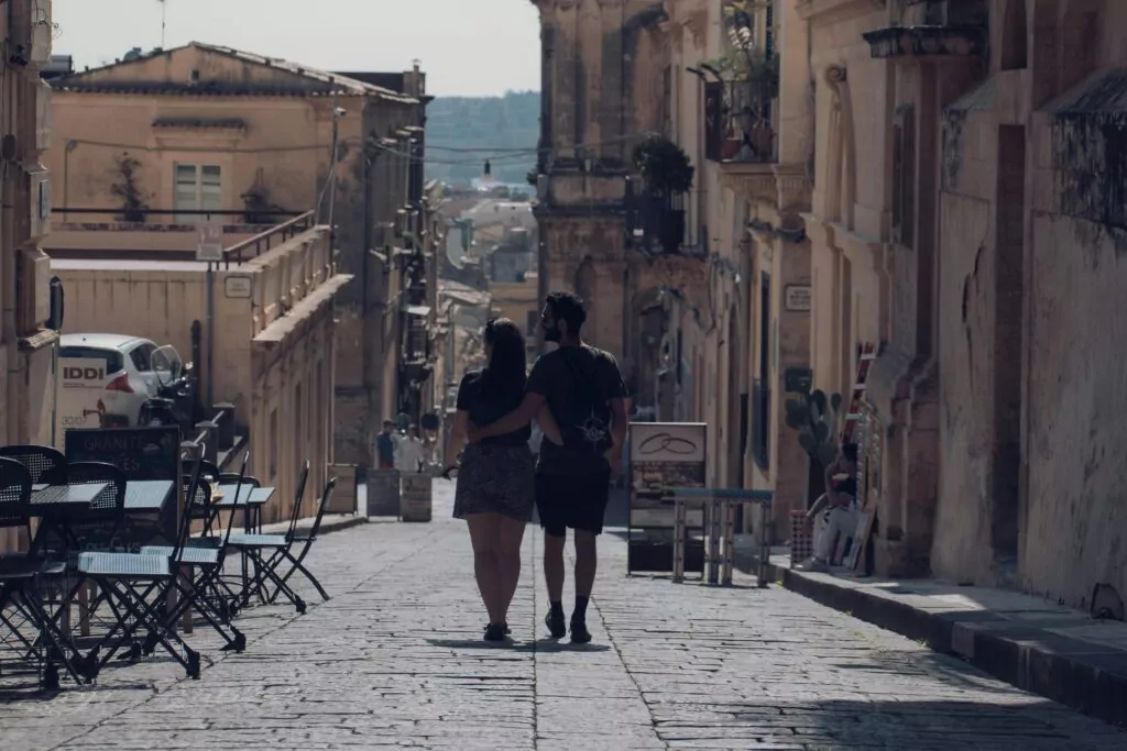 Couple enjoying a romantic walk down a historic street in Noto, Sicily, Italy.