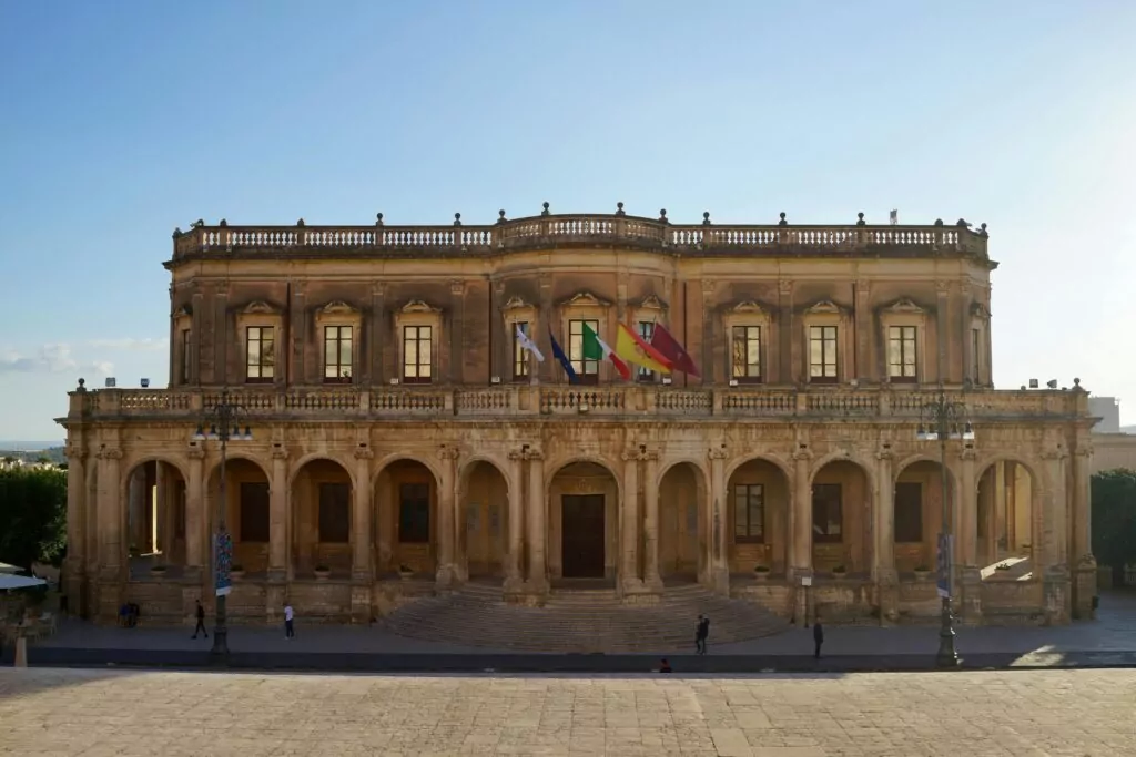 Front view of the famous Palazzo Ducezio in Noto, Sicily, showcasing Baroque architecture under a clear summer sky.