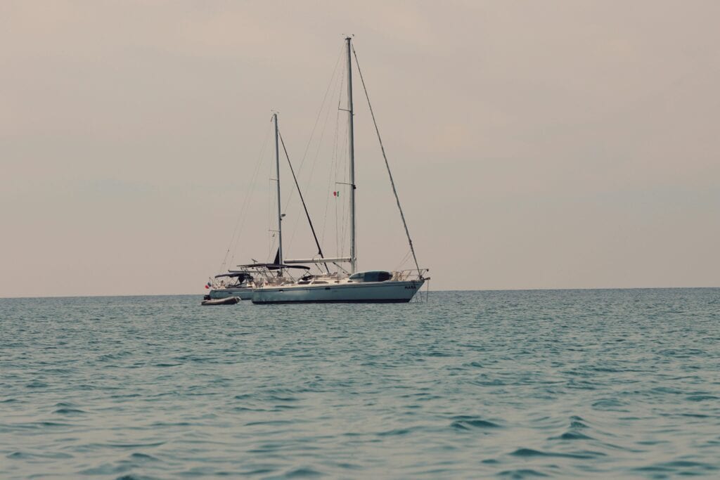 A serene view of a sailboat anchored in the ocean near Cefalù, Sicily.