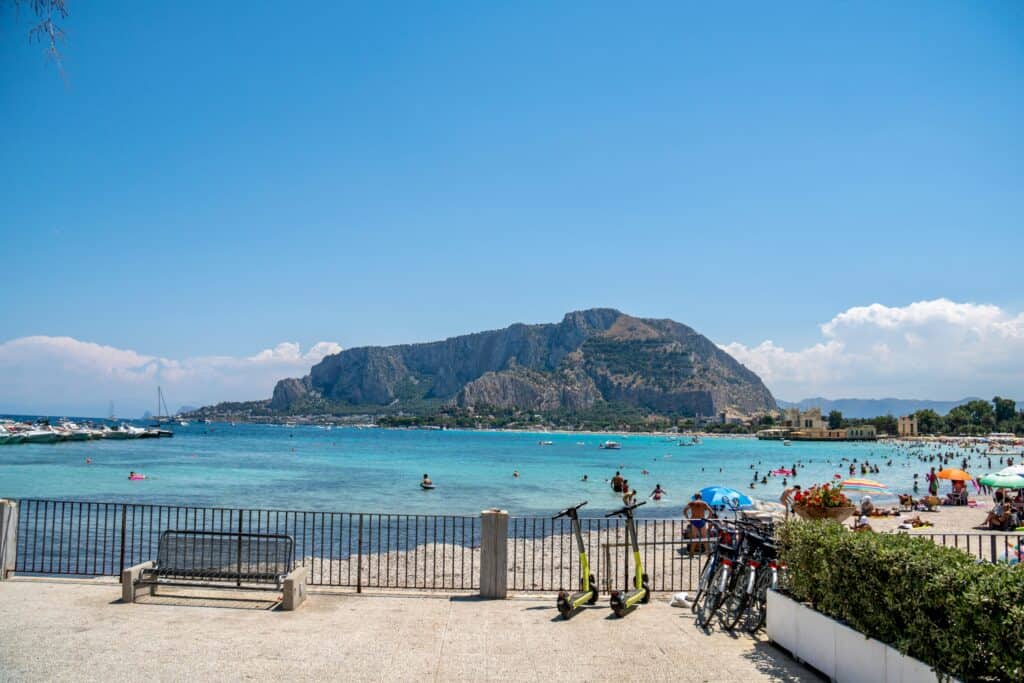 A sunny day at Mondello Beach, Sicily, featuring clear waters, mountains, and leisure activities.