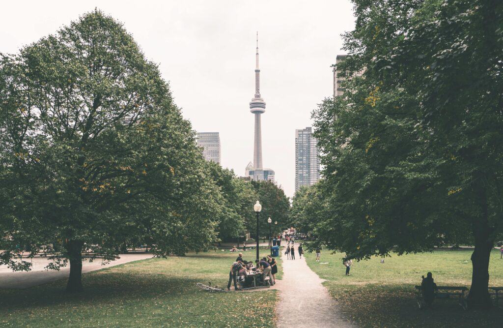 View of Toronto's CN Tower from a park with people enjoying the greenery on an overcast day.