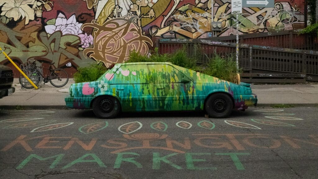 A vibrant painted car art installation in Toronto's Kensington Market with graffiti background.