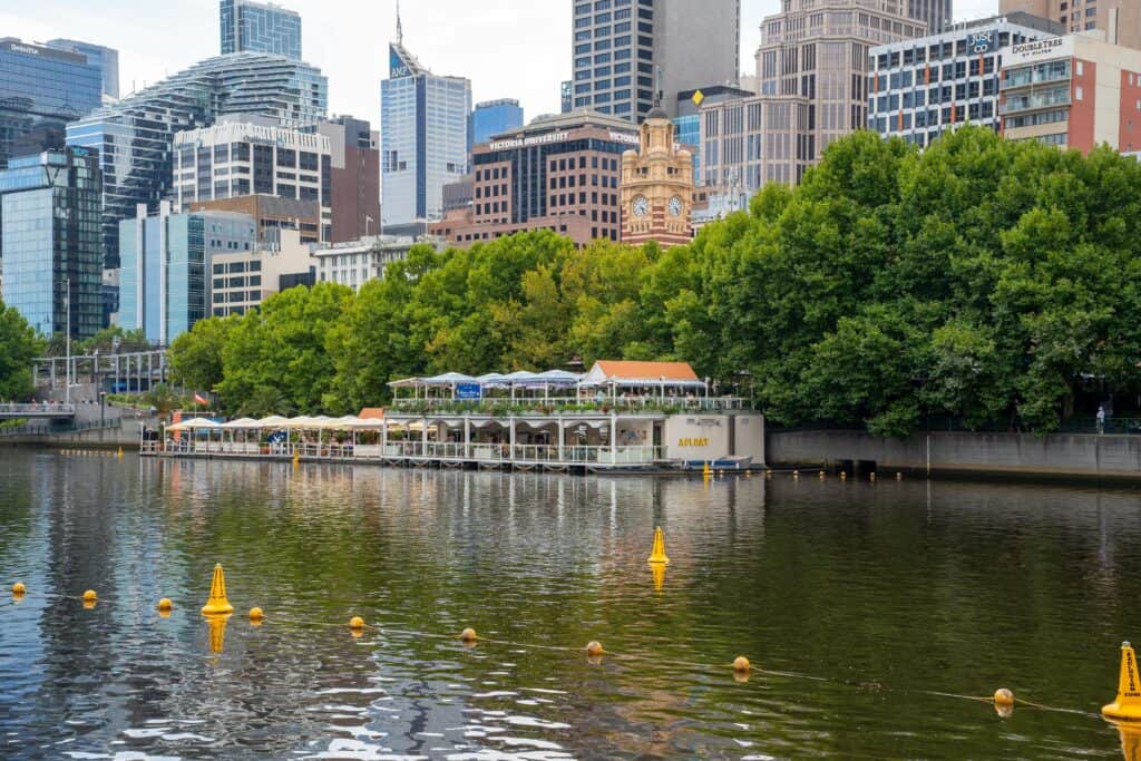 Scenic view of Melbourne's skyline along the Yarra River showcasing the Afloat Bar and lush greenery.