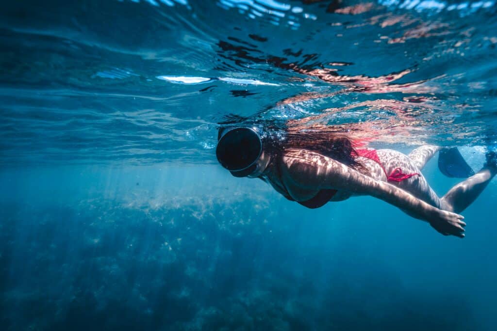 A woman wearing a bikini snorkeling in the clear blue sea of Bahia, Brazil, enjoying underwater exploration.
