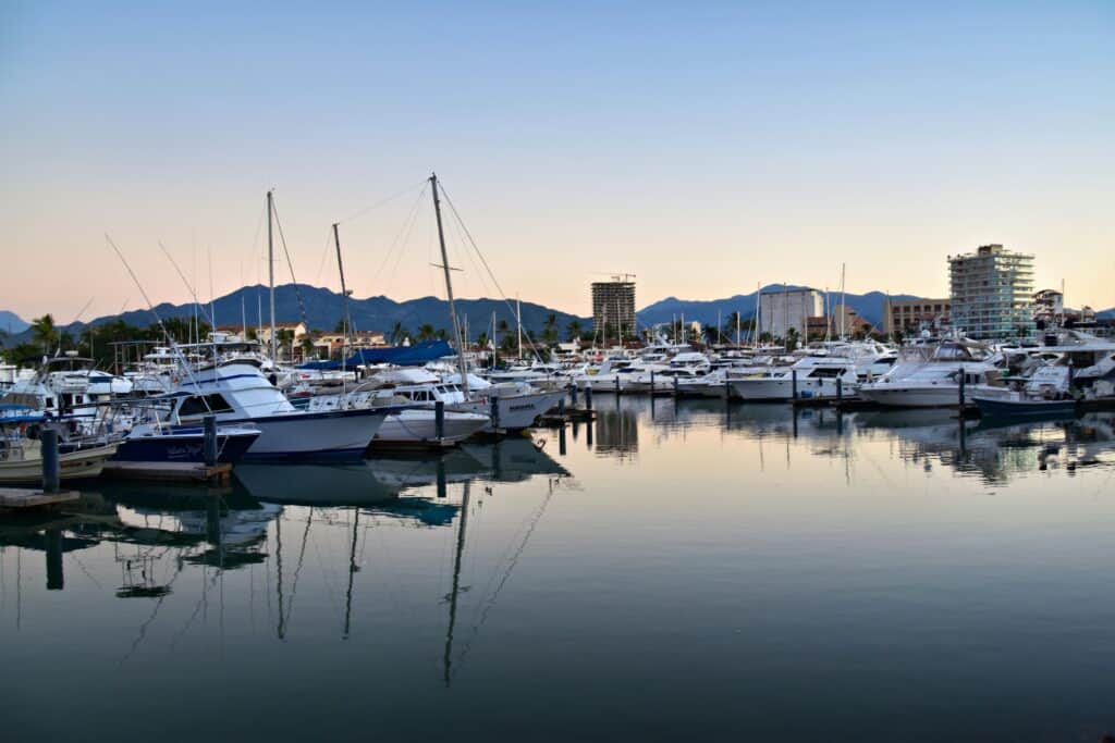 Discover the stunning Puerto Vallarta harbor reflecting yachts at sunset, framed by mountains.