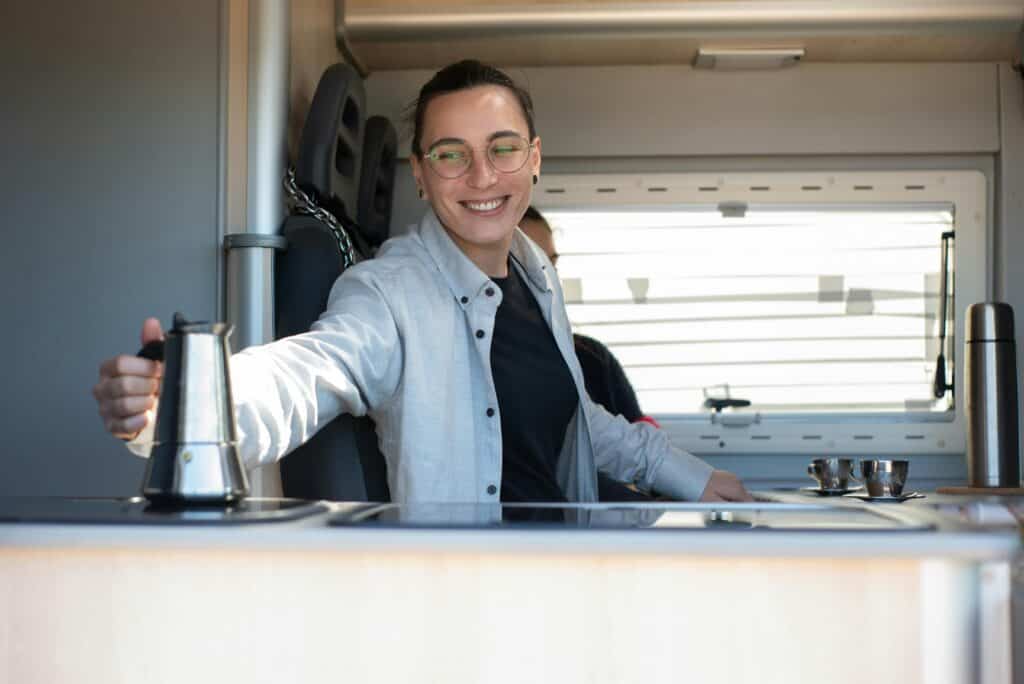 Caucasian person smiling while preparing coffee inside an RV kitchen in Portugal.