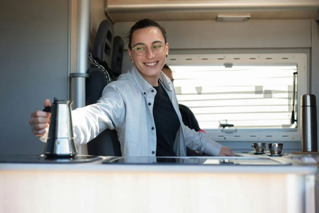Caucasian person smiling while preparing coffee inside an RV kitchen in Portugal.