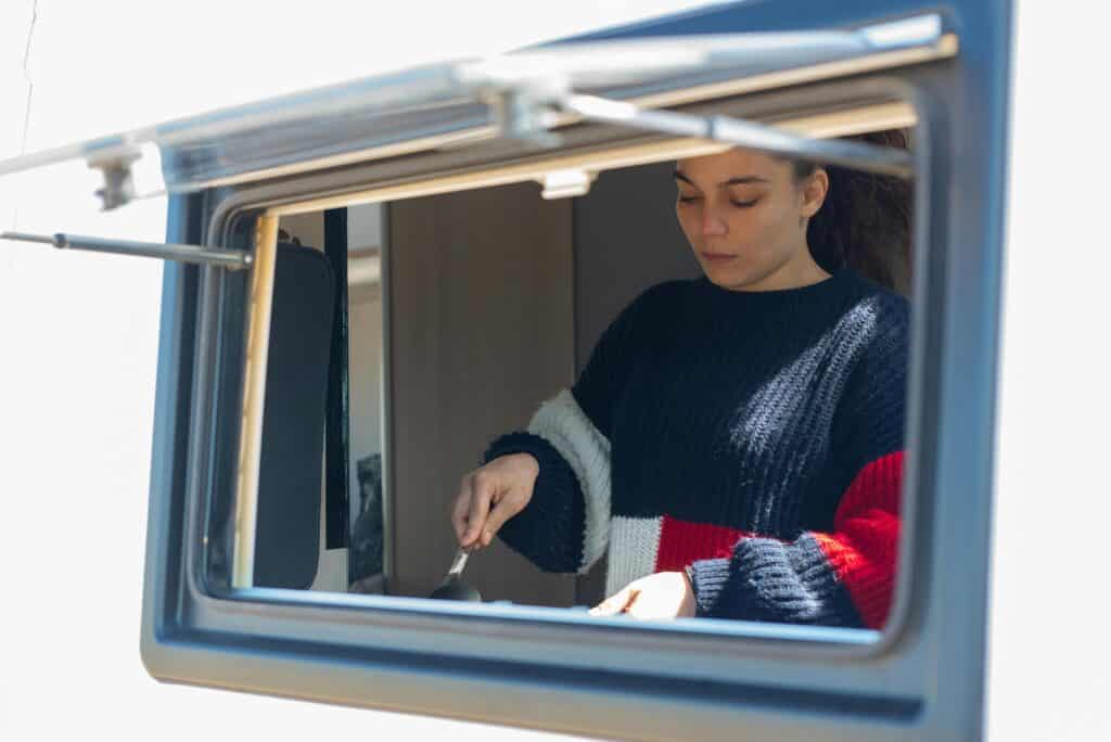 Woman preparing food inside camper van, showcasing mobile living lifestyle.
