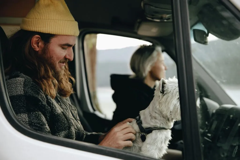 Man and woman enjoy a scenic road trip with their dog in a van.