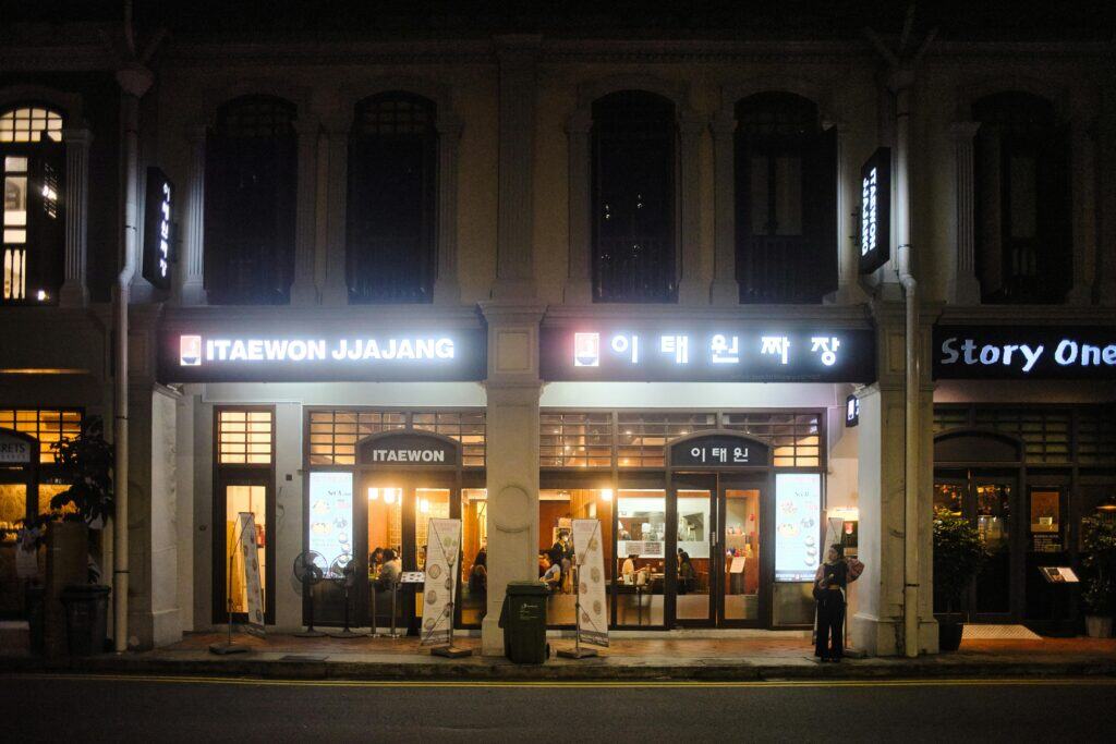Night scene of Itaewon Jjajang restaurant illuminated with signage on a bustling street.