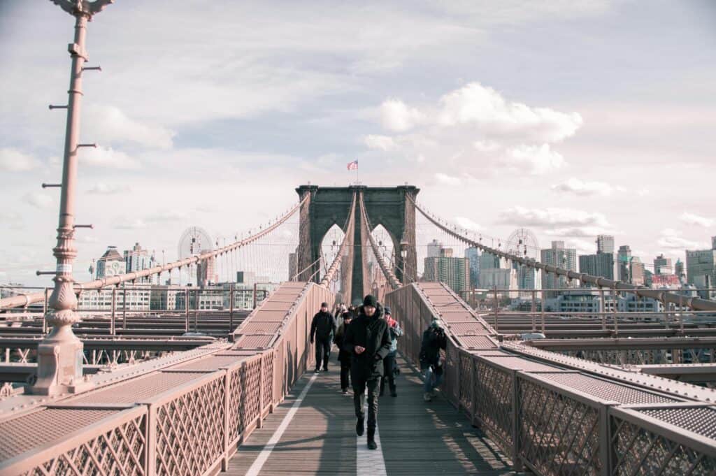 Pedestrians walk along the iconic Brooklyn Bridge with the Manhattan skyline in the background.