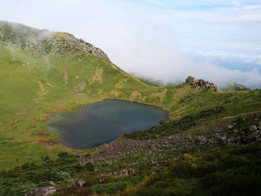 A serene mountain landscape featuring a tranquil lake surrounded by lush greenery and misty clouds.