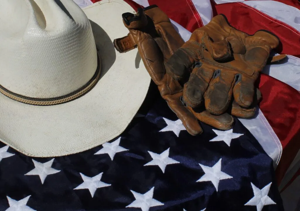 A cowboy hat and gloves resting on an American flag, symbolizing patriotism.