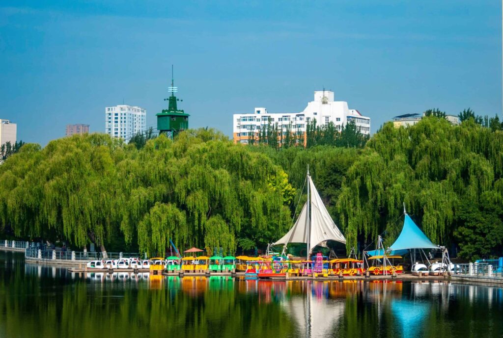 A vibrant urban park featuring colorful boats, lush greenery, and modern skyline.