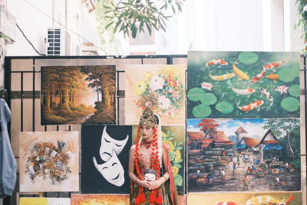 Indonesian dancer in traditional attire surrounded by diverse paintings in West Java.