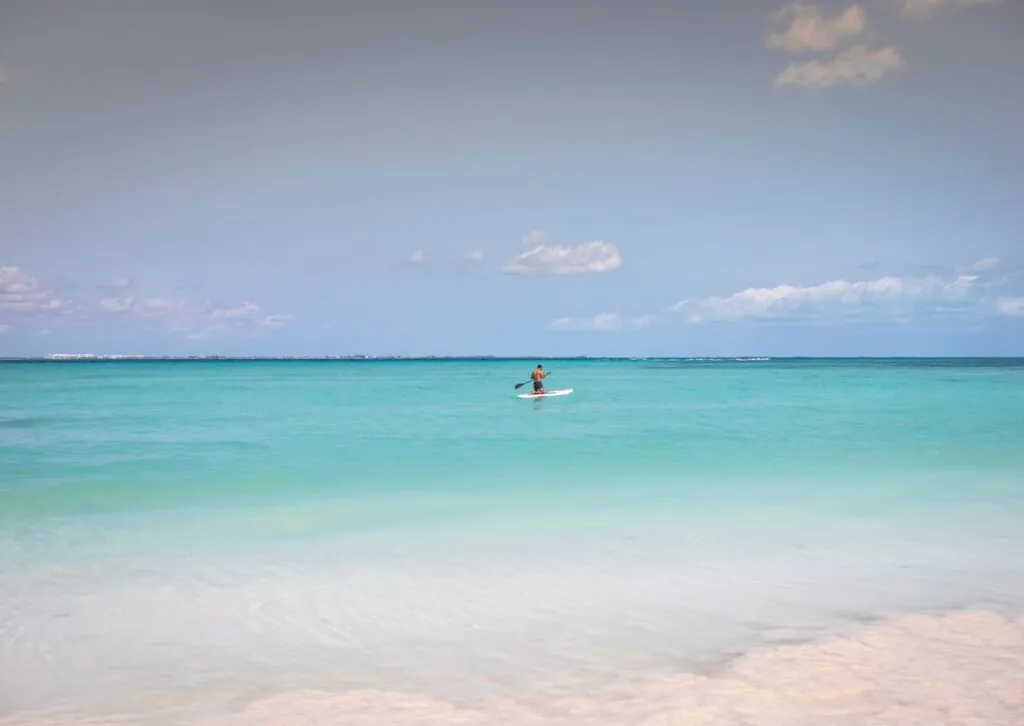 A man enjoys paddleboarding on the serene turquoise waters of Cancún, México under a clear sky.