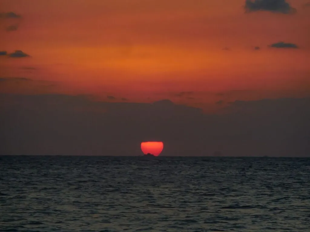 Tranquil beach sunset with a vivid orange sky over a calm sea, ideal for relaxation themes.
