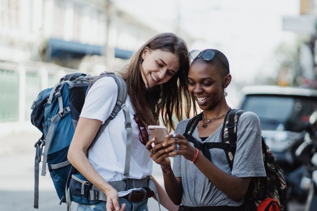 Two diverse women enjoying travel with backpacks, sharing a happy moment on a street.