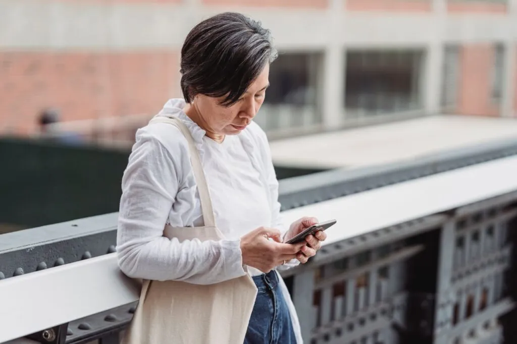 Casual scene of a woman interacting with her smartphone outdoors, leaning on railings.