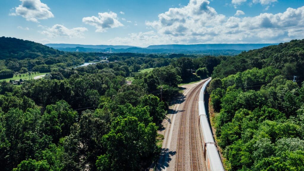 A scenic aerial shot showing railway tracks cutting through verdant forests under a bright blue sky.