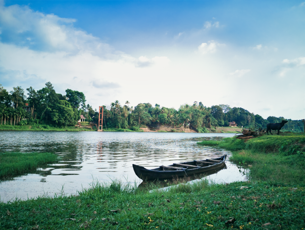 Tranquil riverside scene featuring a traditional boat and lush greenery in Ramamangalam, Kerala.