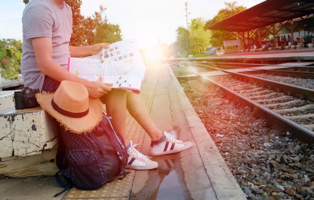 Person sitting at train station platform reading map, embracing travel adventure.
