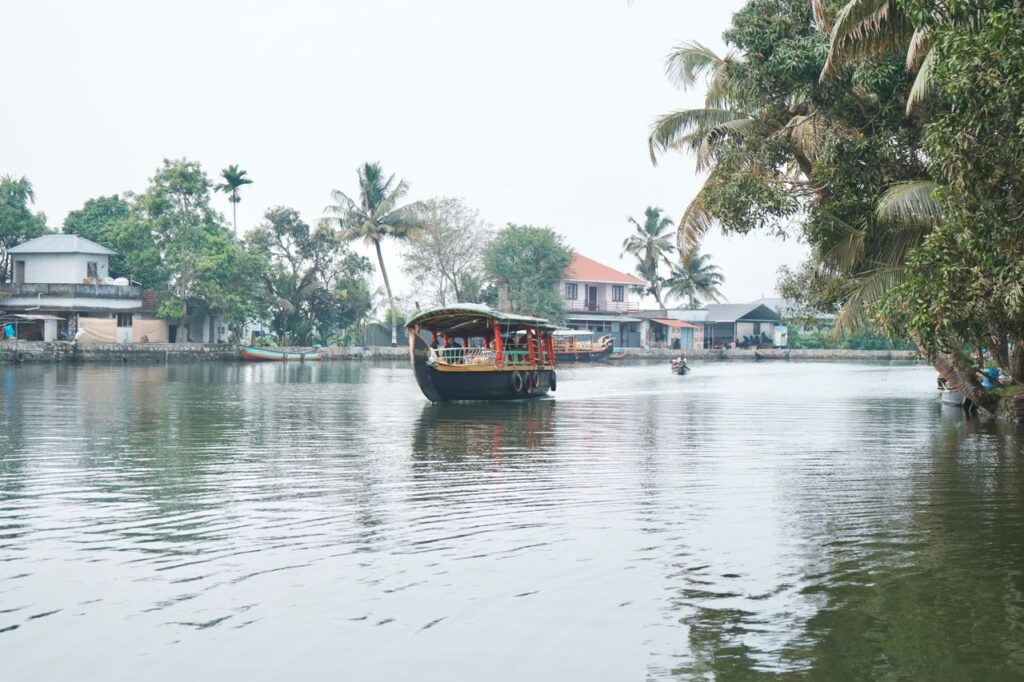 Serene view of a houseboat on Kerala's lush, tranquil backwaters with coconut trees and quaint houses.
