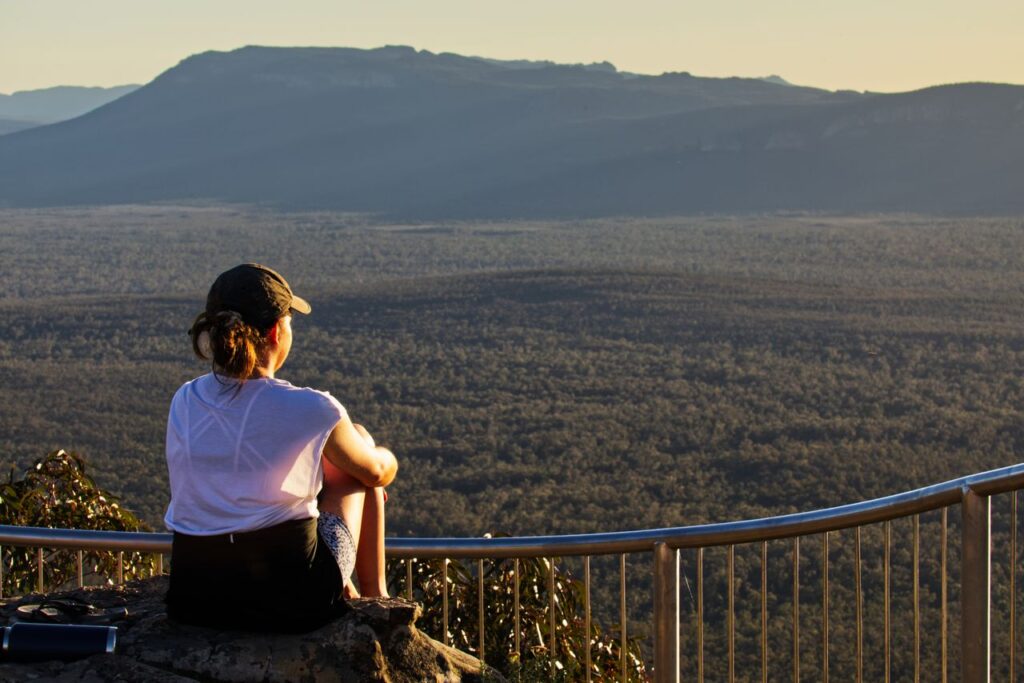 A woman sits on a rock, enjoying the expansive view of the Grampians at sunset.
